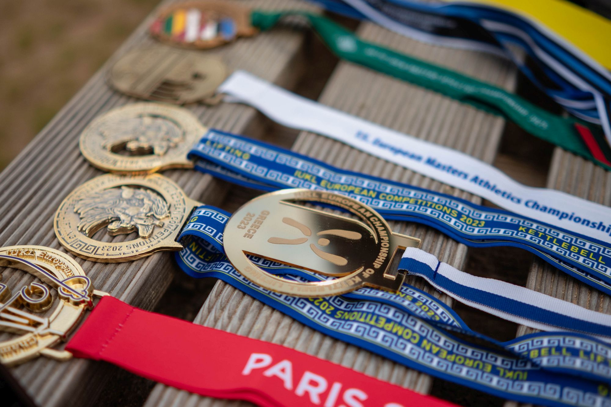Medaļas izliktas uz koka virsmas: lentes, uzraksti European Championships, Paris, Estonia, Latvia.