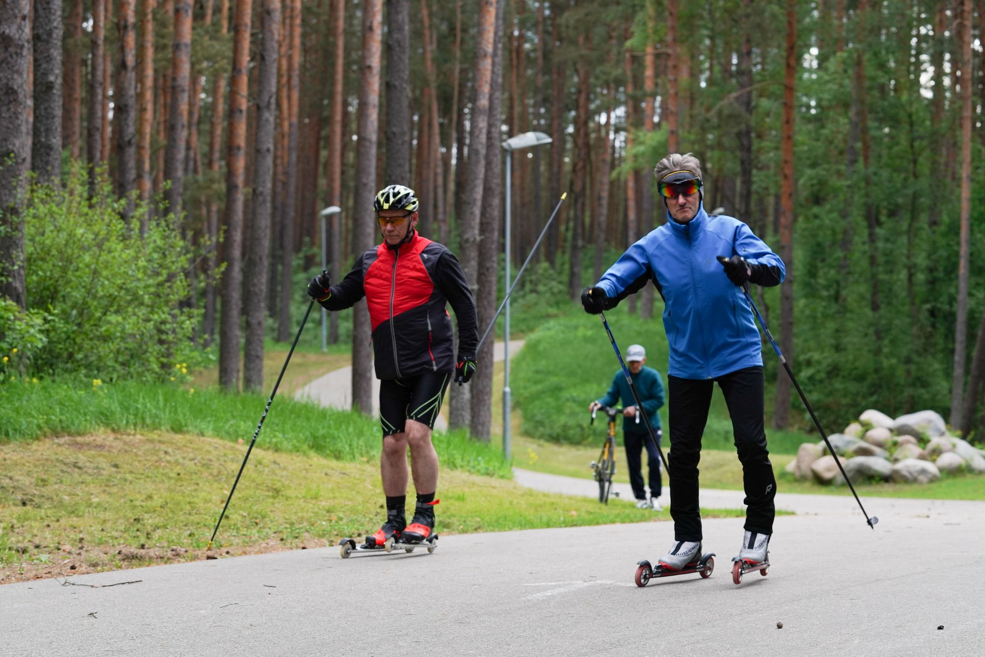 Pjotrs un cits sportists pārvietojas blakus pa trasi; fonā velosipēdists.