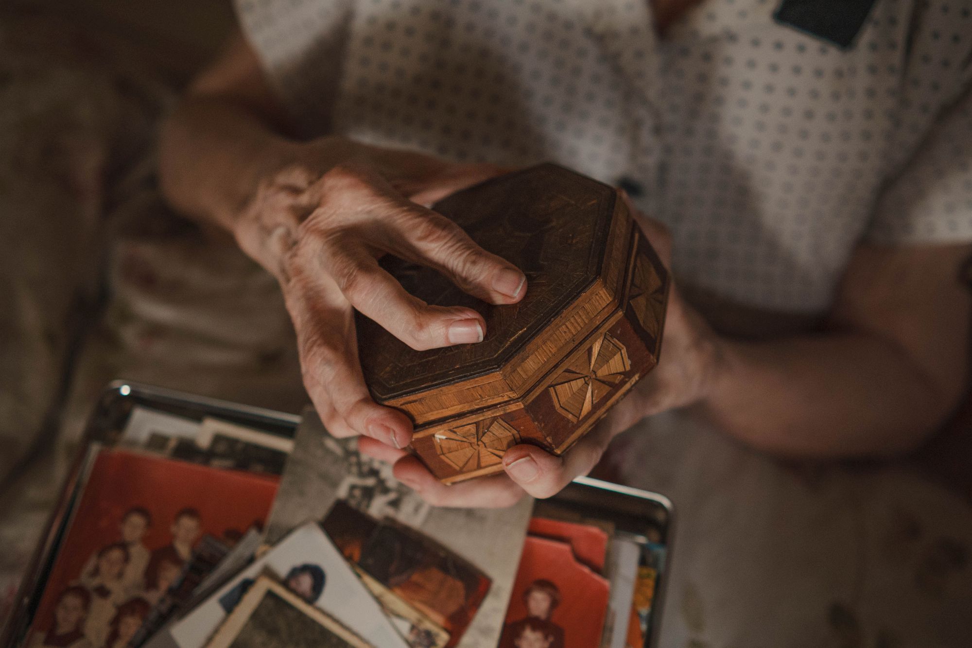 Veronikas rokas tur koka lādīti virs kastes ar fotogrāfijām.